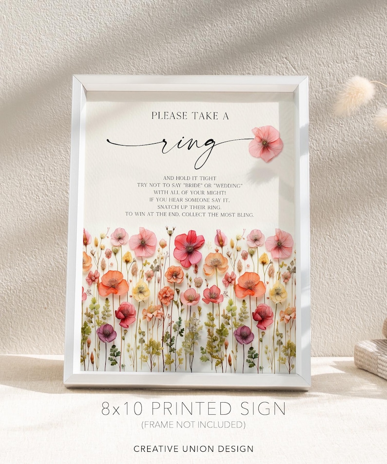 K&ouml;nnte beinhalten: Ein gerahmtes, bedrucktes Schild im Format 20x25 cm mit floralem Design. Auf dem Schild steht "Please Take a Ring" mit Anweisungen f&uuml;r ein Hochzeitsspiel. Der untere Teil des Schildes tr&auml;gt den Text "Creative Union Design".