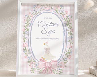 May include: A framed print with a white border features a custom sign design. The sign has a light blue oval frame with floral accents and a pink bow. The text reads "Create any Custom Sign and print as many as you need". A cartoon goose is in the center.