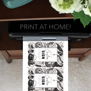 May include: A printer is shown printing two Halloween-themed signs. The signs feature a border of skulls, spiders, and other spooky elements. The text on the signs reads "Custom Sign" and "Print as many as you need". The image also includes the text "Print at Home!"