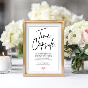 May include: A gold-framed sign with the text "Time Capsule" in black cursive font. The sign instructs guests to write a message to a baby to be opened when the baby turns 18 in 2045.