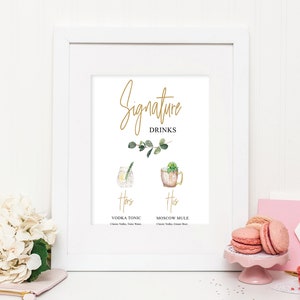 Puede incluir: Un cartel enmarcado en blanco con el texto "Signature Drinks" en letras doradas. El cartel presenta dos ilustraciones de acuarela de c&oacute;cteles, etiquetados como "Hers" y "His". El c&oacute;ctel "Hers" es un Vodka Tonic y el c&oacute;ctel "His" es un Moscow Mule.
