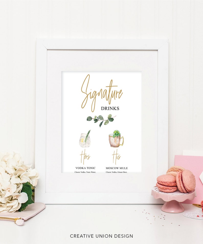 Puede incluir: Un cartel enmarcado en blanco con el texto "Signature Drinks" en letras doradas. El cartel presenta dos ilustraciones de acuarela de c&oacute;cteles, etiquetados como "Hers" y "His". El c&oacute;ctel "Hers" es un Vodka Tonic y el c&oacute;ctel "His" es un Moscow Mule.