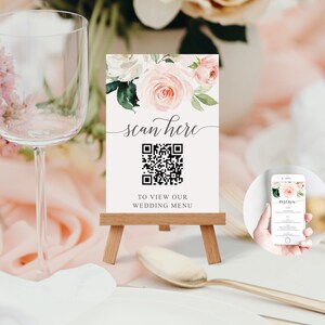 Op de afbeelding: Een witte kaart met een bloemenontwerp en een QR-code. De kaart zegt "scan here" en "to view our wedding menu".