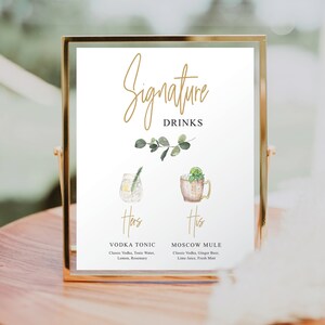 Puede incluir: Un cartel con marco dorado con el texto "Signature Drinks" en escritura dorada. El cartel presenta dos ilustraciones de acuarela de c&oacute;cteles, una etiquetada como "Hers" y la otra como "His". El c&oacute;ctel "Hers" es un vodka tonic con romero y el c&oacute;ctel "His" es un Moscow mule con una rodaja de lima y menta.