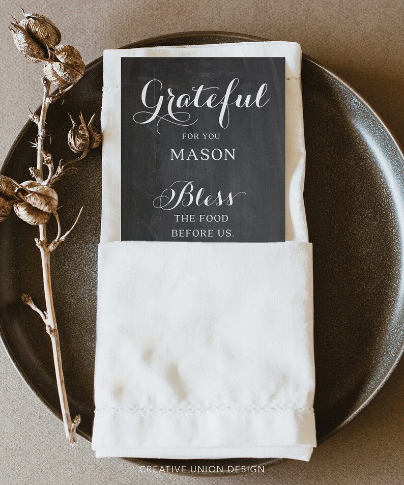 Puede incluir: Un cubierto con un plato gris oscuro, una servilleta de lino blanca y una tarjeta negra con escritura blanca que dice "Grateful for you Mason Bless the food before us". Un tallo de planta seca est&aacute; a la izquierda.