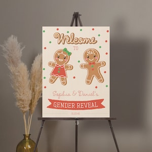 May include: A gender reveal sign on an easel. The sign features two gingerbread people, one in a red dress and the other with a bow tie. The text reads "Welcome to Sophia & Daniel's Gender Reveal" with the date 01.23.45.