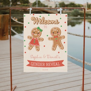 May include: A gender reveal sign featuring gingerbread people. The sign reads "Welcome to Sophia & Daniel's Gender Reveal" with the date 01.23.45. The sign is decorated with red and green polka dots and is held by a copper stand.