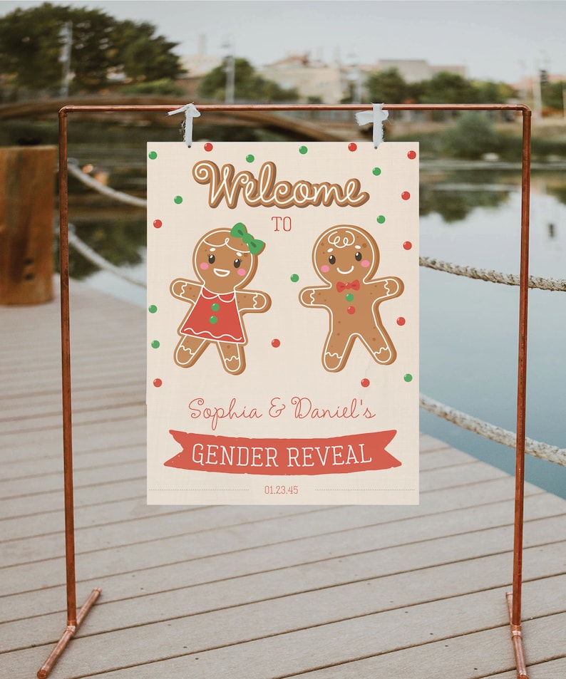 May include: A gender reveal sign featuring gingerbread people. The sign reads "Welcome to Sophia & Daniel's Gender Reveal" with the date 01.23.45. The sign is decorated with red and green polka dots and is held by a copper stand.