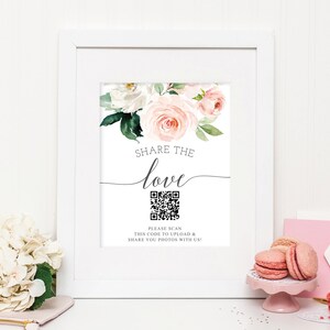 K&ouml;nnte beinhalten: Wei&szlig; gerahmtes Schild mit floralen Akzenten und dem Text "SHARE THE love". Enth&auml;lt einen QR-Code und den Text "PLEASE SCAN THIS CODE TO UPLOAD & SHARE YOU PHOTOS WITH US!". Das Schild ist mit rosa Rosen und wei&szlig;en Blumen verziert.