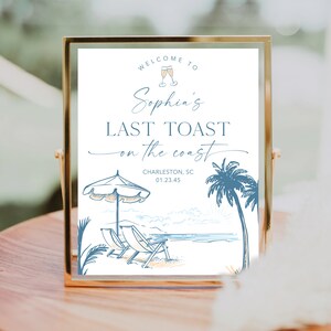 May include: A white sign with blue text that reads "Welcome to Sophia's Last Toast on the Coast". The sign also includes the text "Charleston, SC 01.23.45" and a drawing of a beach scene with palm trees, beach chairs, and an umbrella.