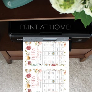 May include: Two printable baby bingo cards with a floral design. The cards feature a pink and white floral pattern with the words "Baby Bingo" at the top. The cards are filled with squares containing baby-related words like "diaper", "blanket", and "gift card".