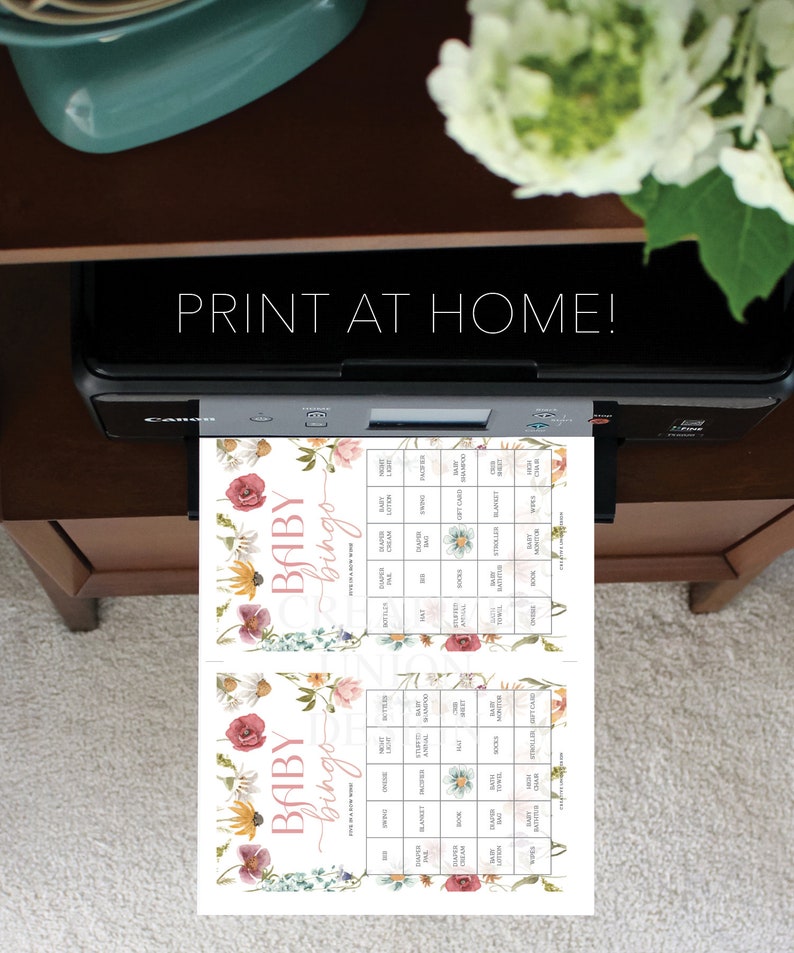 May include: Two printable baby bingo cards with a floral design. The cards feature a pink and white floral pattern with the words "Baby Bingo" at the top. The cards are filled with squares containing baby-related words like "diaper", "blanket", and "gift card".