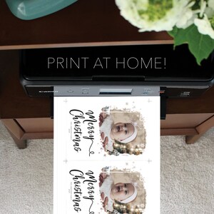 May include: A printer is shown printing two Christmas cards with a baby's photo. The cards have the text "Merry Christmas" in a script font. The image also includes the text "PRINT AT HOME!" and the words "CREATIVE UNION DESIGN".