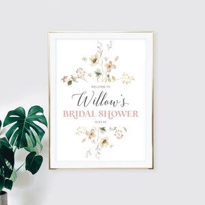 May include: A framed print with a gold border, featuring the text "Welcome to Willow's Bridal Shower" in elegant script and a soft pink color. The design includes watercolor floral elements in muted tones, creating a delicate and romantic aesthetic.