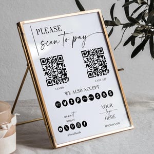 May include: A gold-framed sign with the text "PLEASE scan to pay" and two QR codes for Venmo and Cash App. The sign also lists accepted payment methods and social media icons. The sign is propped up on a gold stand.