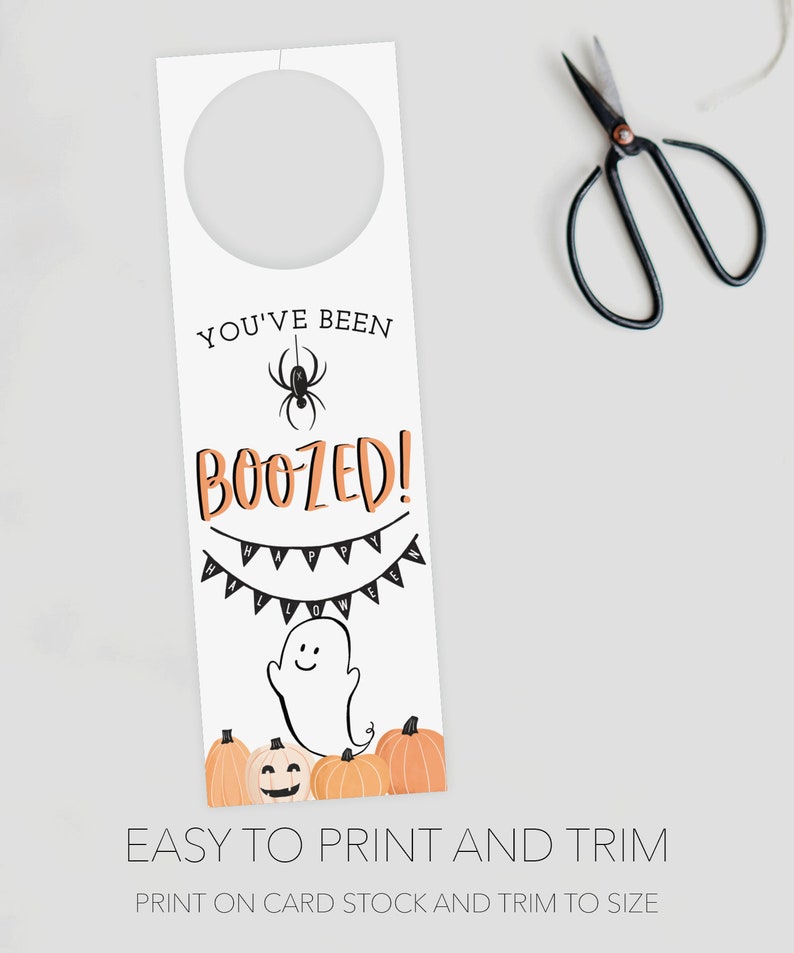 K&ouml;nnte beinhalten: Ein wei&szlig;er T&uuml;rh&auml;nger zum Thema Halloween mit einem kreisf&ouml;rmigen Ausschnitt oben. Das Design enth&auml;lt den Text "YOU'VE BEEN BOOZED!" mit einer Spinne, einem Banner mit der Aufschrift "HALLOWEEN", einem Geist und K&uuml;rbissen. Schwarze Scheren sind im Hintergrund.
