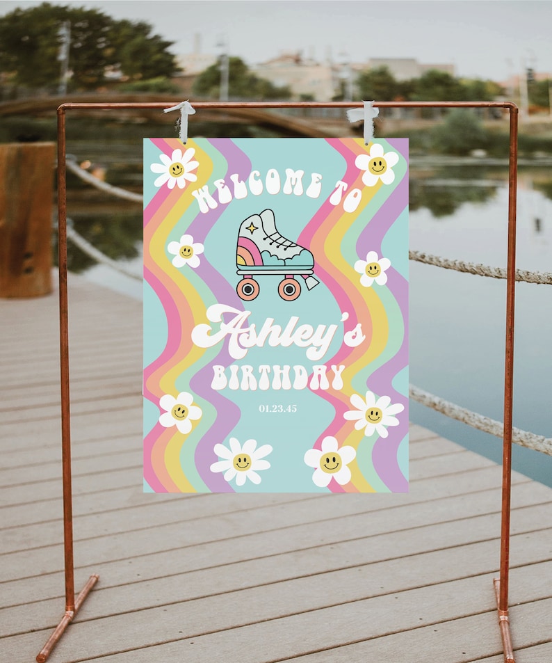K&ouml;nnte beinhalten: Willkommen zum Geburtstag von Ashley Schild mit Regenbogenhintergrund und einem Rollschuh-Motiv. Das Schild hat einen blauen Hintergrund mit wei&szlig;en G&auml;nsebl&uuml;mchen und einem gelben Smiley.