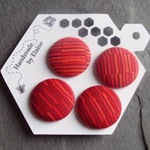 Peut inclure: Quatre boutons en tissu rayés rouge et orange sur une carte blanche avec le texte "Handmade by Elaine".