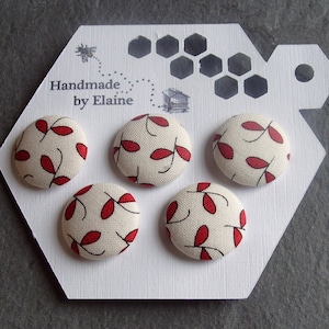 Peut inclure: Quatre boutons en tissu blanc avec des motifs de feuilles rouges. Les boutons sont présentés sur une carte hexagonale blanche avec le texte "Handmade by Elaine".