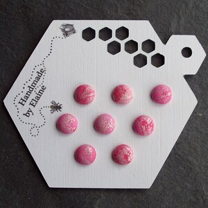 May include: A white card with the text "Handmade by Elaine" and a bee illustration. The card has seven pink fabric buttons with a white pattern arranged in a circle.