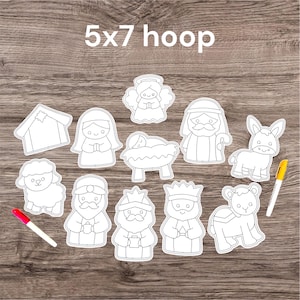 May include: A collection of white, outline-style Christmas nativity figures, including Mary, Joseph, baby Jesus, an angel, and the three wise men. The text "5x7 hoop" is at the top. Two markers are on the wooden surface.