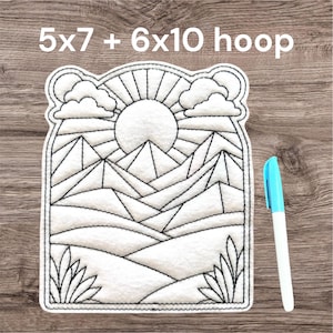 May include: White and black embroidered mountain scene with a sun and clouds. The text "5x7 + 6x10 hoop" is at the top. A blue and white marker is on the right side.