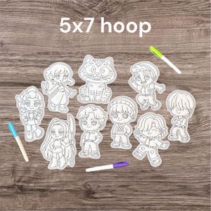 Pode incluir: Uma coleção de recortes de personagens brancos e um recorte de gato, com três marcadores coloridos. O texto "5x7 hoop" é exibido no topo. Os recortes estão dispostos sobre uma superfície de madeira.