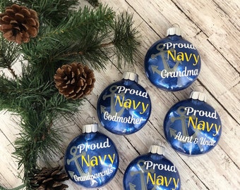 May include: Five blue Christmas ornaments with glitter and a gold anchor design. Each ornament has white text that reads "Proud Navy" followed by a title such as "Godmother", "Grandparents", "Grandma", and "Aunt & Uncle".