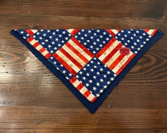 May include: A blue and red bandana with a checkered pattern of stars and stripes. The bandana is folded into a triangle shape.