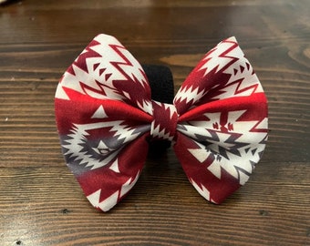 May include: A red, white, and gray bow tie with a geometric pattern. The bow tie is made of fabric and has a black elastic band.