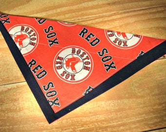 May include: Red and black bandana with the Boston Red Sox logo. The bandana is made of a red fabric with a black border and features the Boston Red Sox logo in a white circle with the words "Red Sox" and "Boston" in black.