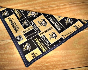 May include: A black and gold fabric triangle with the Pittsburgh Penguins logo repeated throughout. The fabric is sewn with a dark blue trim.