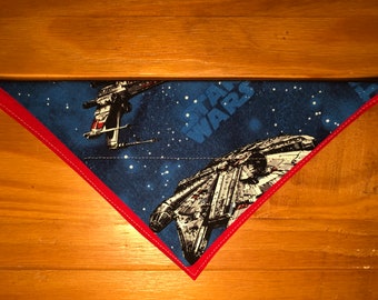 May include: A blue and red triangular fabric bandana with a Star Wars theme. The bandana features a white spaceship and the text "Star Wars" in white letters.