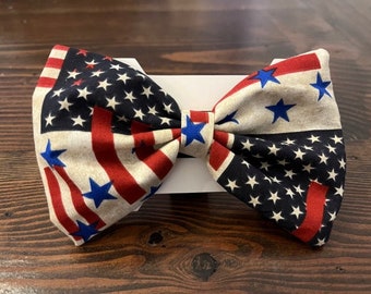 May include: A red, white, and blue bow tie with a distressed American flag pattern. The bow tie is made of fabric and has a blue star design.