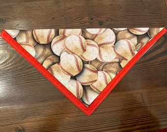 May include: A red and white triangular bandana with a baseball pattern. The bandana is made of fabric and has a red border.