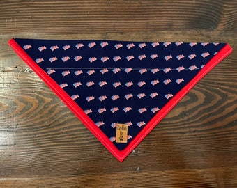 May include: A blue bandana with a white and red American flag pattern. The bandana has a red border and a small brown leather tag with the text "Pawkids Pet" on it.