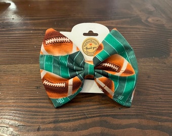 May include: Green and brown bow with a football field and football pattern. The bow has a small white tag that says "Thank you".