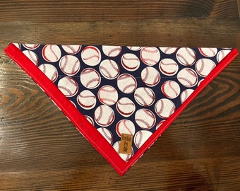 May include: A blue and white bandana with a red trim and a baseball pattern. The bandana has the text "Pawsitive Pet" in the lower right corner.