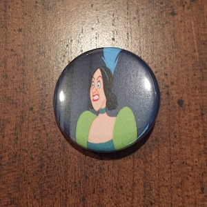 May include: A round button with a cartoon image of a woman with dark hair and a green and blue dress. She has a surprised expression on her face.