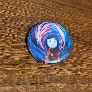 May include: A round button with a colorful image of a girl with dark hair and a red scarf standing in front of a swirling blue and pink background.