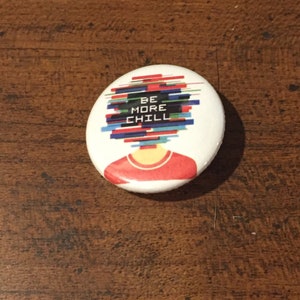 May include: A white button with a red, yellow, and blue design. The design features a person with a head made of colorful lines and the text "BE MORE CHILL".