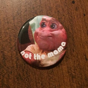 May include: A pink button with a picture of a character from the show "Barney" with the text "Not the mama" on it.