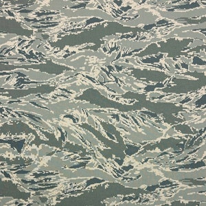 May include: A close-up of a camouflage pattern fabric with a blend of green, white, and blue colors. The pattern resembles a series of abstract waves.