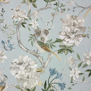 Puede incluir: Tela azul claro con un diseño floral y de aves. El patrón incluye peonías blancas y grises, campanillas azules y pájaros posados en ramas. También hay mariposas en el diseño.