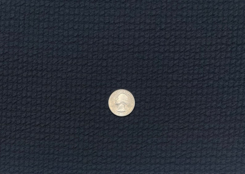 May include: A silver US quarter coin on a dark blue textured surface.