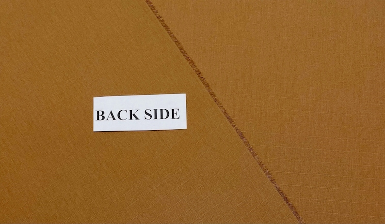 May include: Close-up of a piece of tan fabric with a diagonal seam. A white rectangle with the words "BACK SIDE" is in the centre of the image. The fabric has a textured appearance.