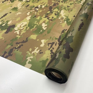 May include: A roll of camouflage fabric in a green, brown, and tan pattern. The fabric is rolled up and the end of the roll is visible.