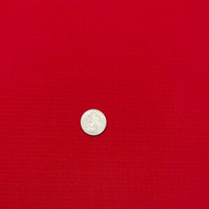 May include: A close-up of a solid red fabric with a subtle textured pattern. A silver coin is placed in the center of the fabric.