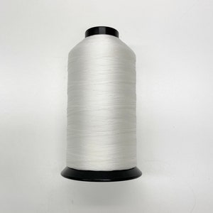 May include: A large spool of white thread with a black base and top. The thread is tightly wound, creating a cylindrical shape. The image is a close-up shot against a white background, highlighting the texture and color of the thread.