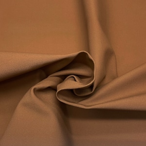 Puede incluir: Primer plano de una muestra de tela de color beige. La tela está tejida de forma apretada y tiene un ligero brillo. Los pliegues y las curvas crean sombras y reflejos, añadiendo profundidad y textura. El aspecto general es suave y uniforme.